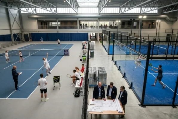 Large indoor sports facility with tennis courts and padel courts in use